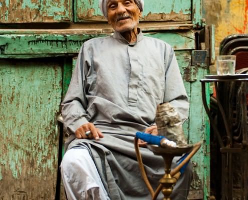 Old Egyptian man sits at a street cafe smoking sheesha in Islamic Cairo